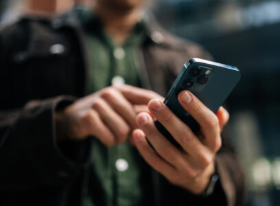 Close-up hands of unrecognizable man holding and using smartphone standing on city street, browsing internet, checking social media, using mobile application. Concept of modern communication.