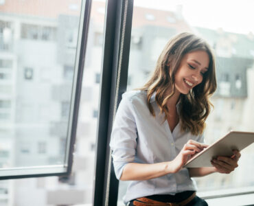 Young businesswoman using a digital tablet while standing in front of windows in office