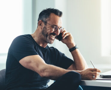 Smiling mature man talking on cell phone and working on his digital tablet. Cheerful businessman working in office.