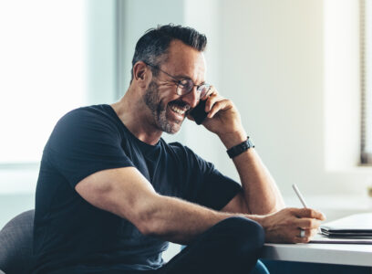 Smiling mature man talking on cell phone and working on his digital tablet. Cheerful businessman working in office.