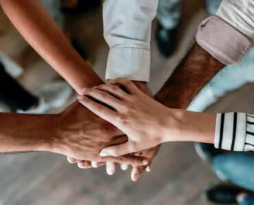 Cooperation. Top view of people holding hands together while standing in the office. Teamwork