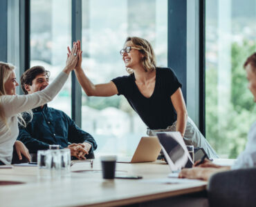 Female professional giving a high five to her colleague in conference room. Group of colleagues celebrating success in a meeting.