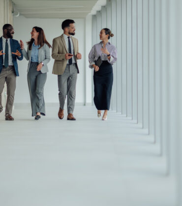 Four businesspeople walking through a modern office hallway, discussing work and collaborating