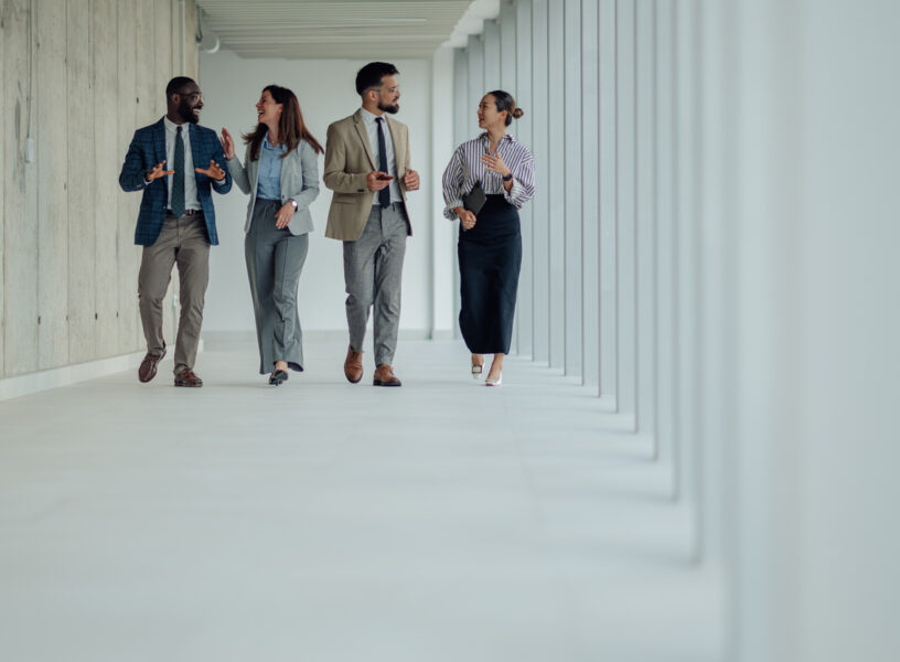 Diverse businesspeople walking and talking in modern office hallway Four businesspeople walking through a modern office hallway, discussing work and collaborating
