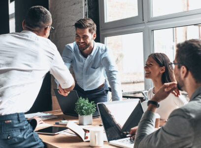Young modern men in smart casual wear shaking hands and smiling while working in the creative office