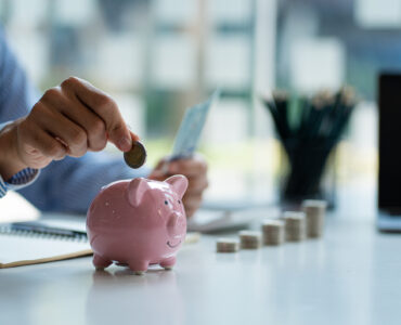 Hands of a young Asian businessman Man putting coins into piggy bank and holding money side by side to save expenses A savings plan that provides enough of his income for payments.