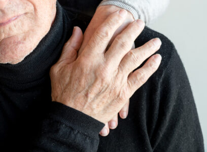 Older  man's hand covering older woman's hand on his shoulder (cropped)