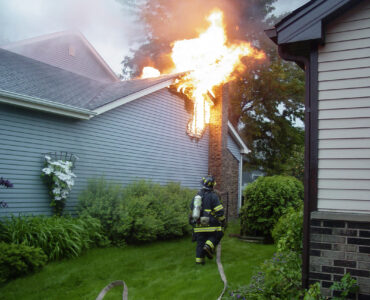 The roof of a house is burning, while a firefighter rushes with his hose to put out the blaze.