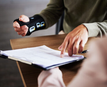 Injury, compensation and man hands with insurance documents, legal contract and paperwork. Disability, accident and people in lawyer or attorney meeting for advice, agreement or policy report closeup