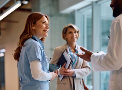 Happy nurse and African American doctor talking to a businesswoman in hallway of a medical clinic.