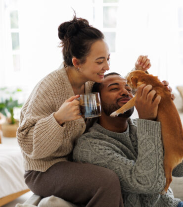 Cheerful young interracial couple with coffee playing with chihuahua dog at home